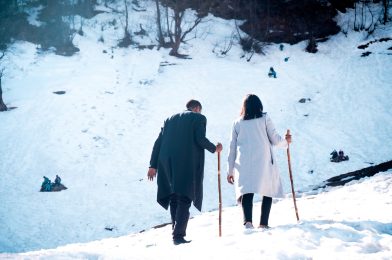 Back view of a couple in coats hiking up the snowy hill in the Solang Valley